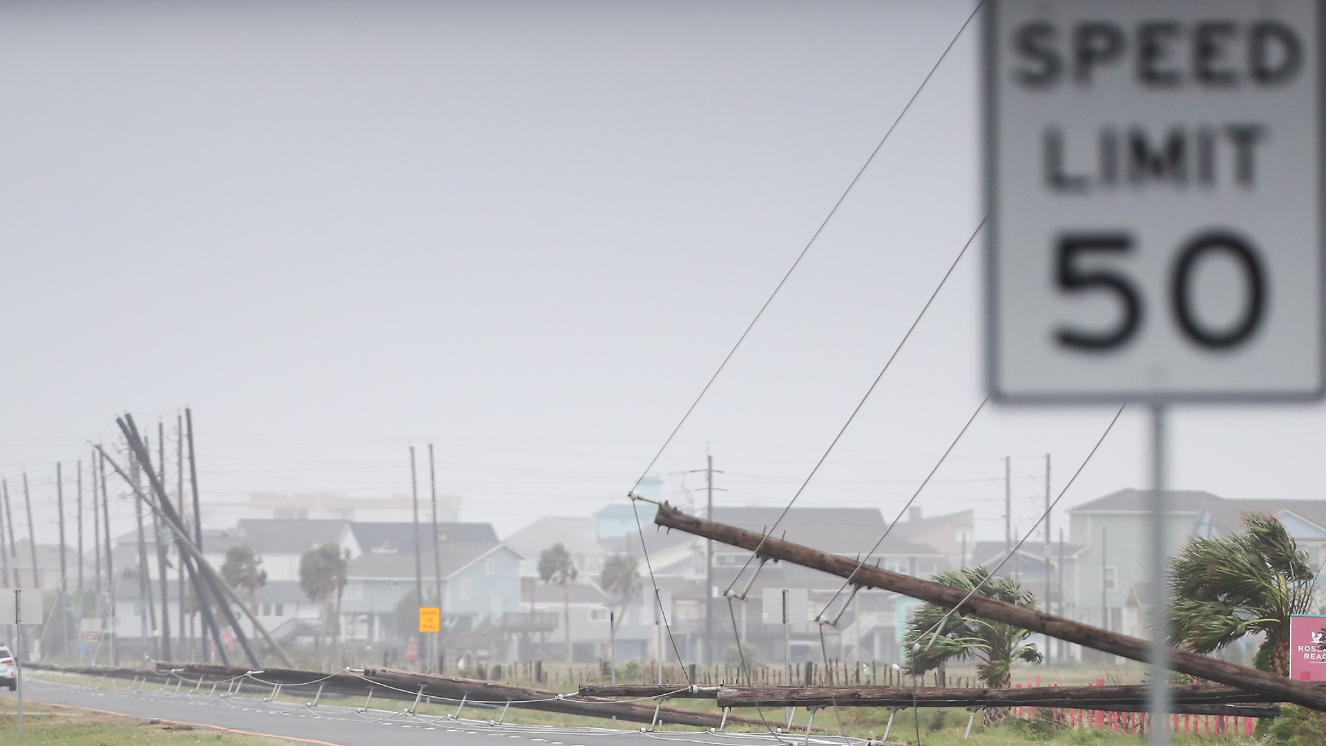 flood waters cover city streets as fallen power lines and damaged buildings can be seen in the background