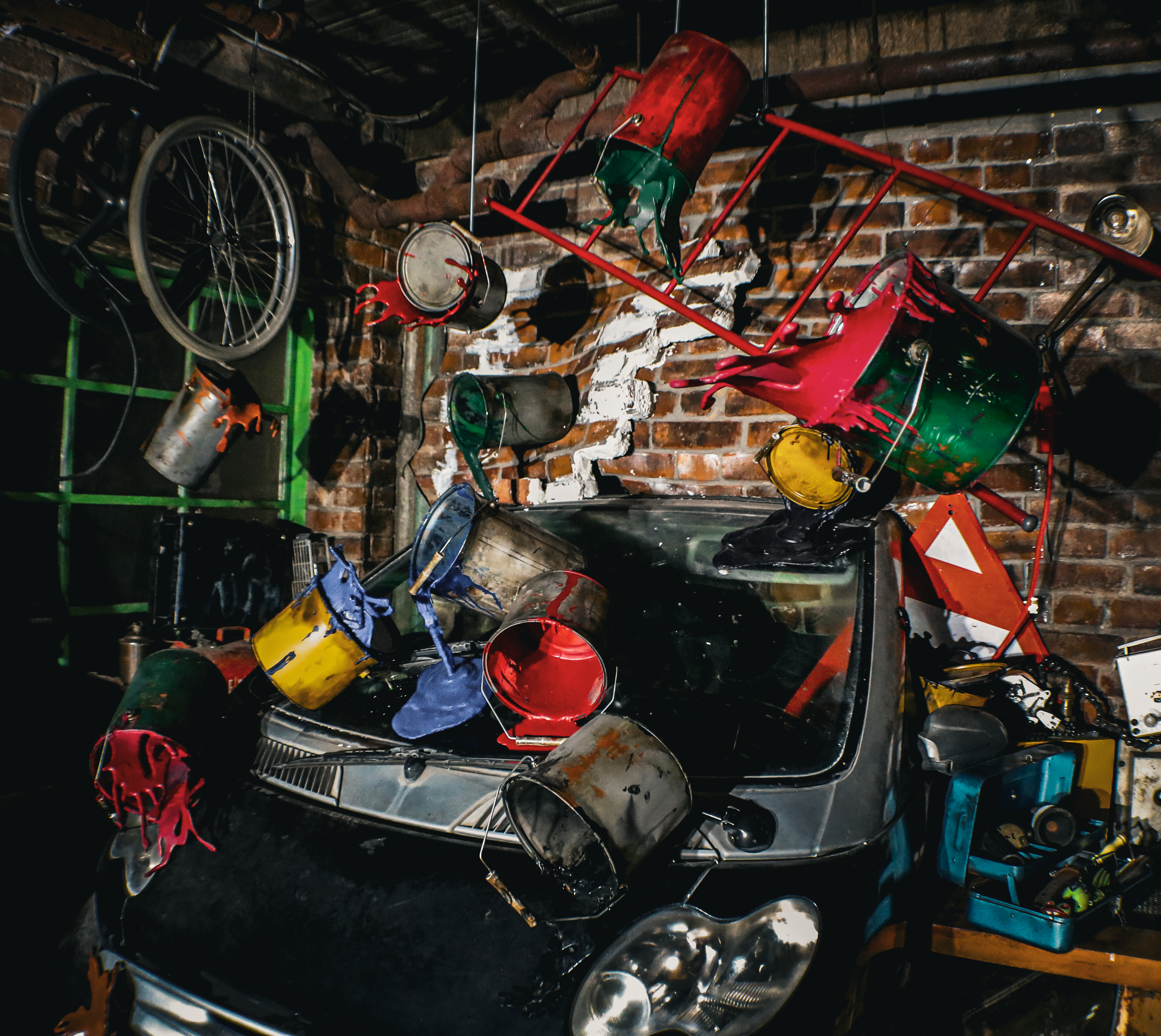 an image of one of the installations in Absurd City showing a car bumper emerging from a brick wall with loads of buckets of different coloured paint thrown across it and the wall behind