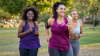 Three women smiling and running through the park