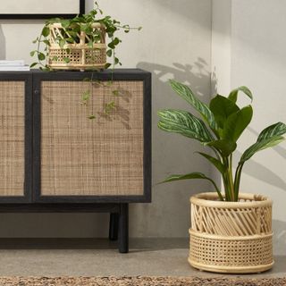 Wooden sideboard with bamboo planter with plant on on floor next to another bamboo planter with plant inside