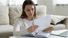 Woman sitting in front of her laptop at a coffee table at home studying a student loan bill