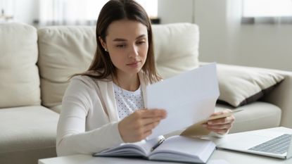 Woman sitting in front of her laptop at a coffee table at home studying a student loan bill 