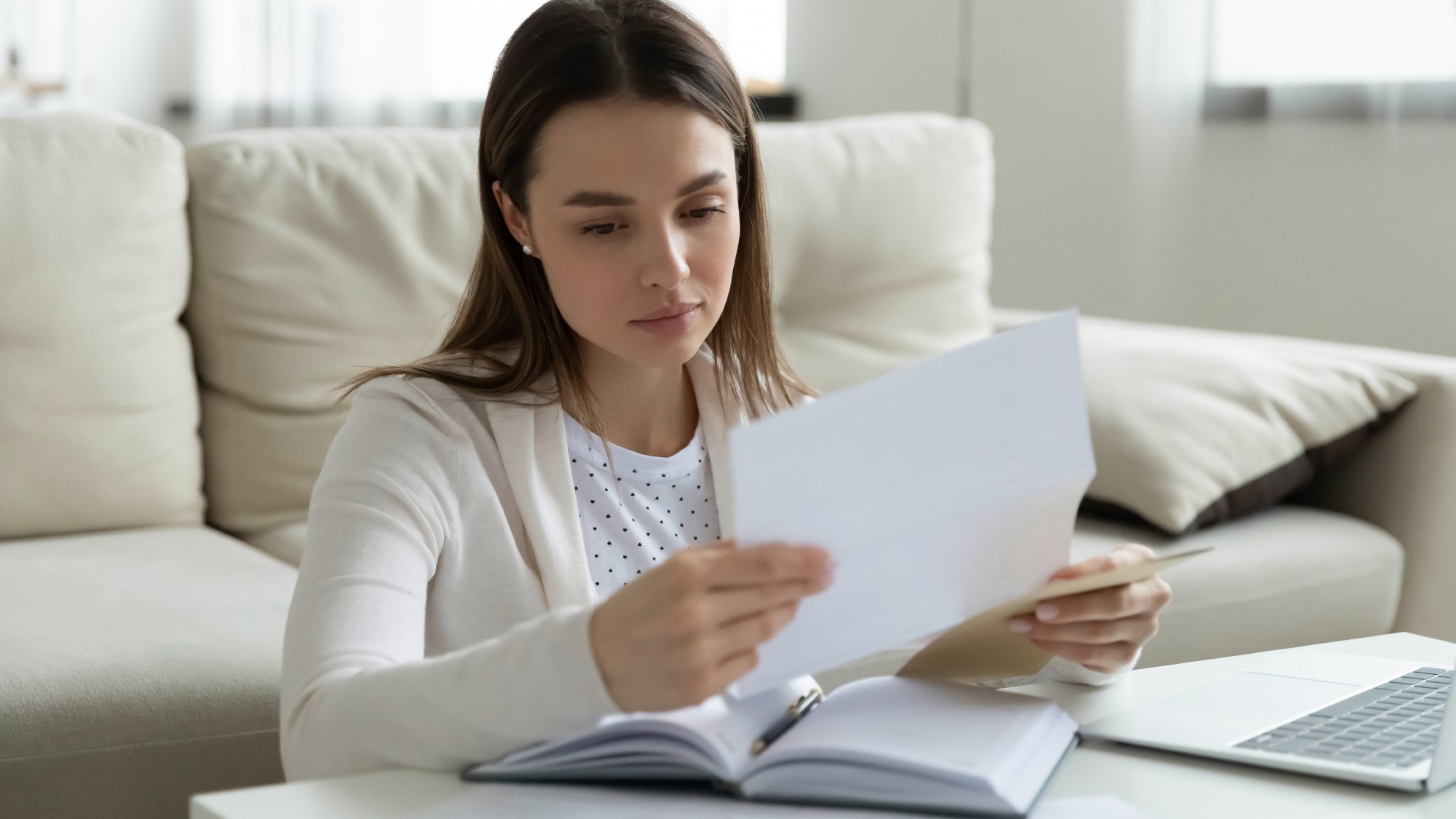 Woman sitting in front of her laptop at a coffee table at home studying a student loan bill 