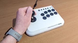 Hori Fighting Stick Mini placed on desk surface with hand on joystick