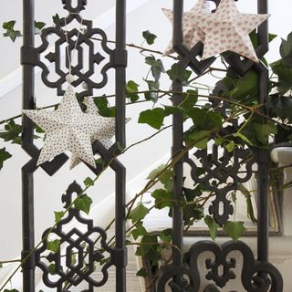 Black staircase railing decorated with strands of green ivy and paper stars