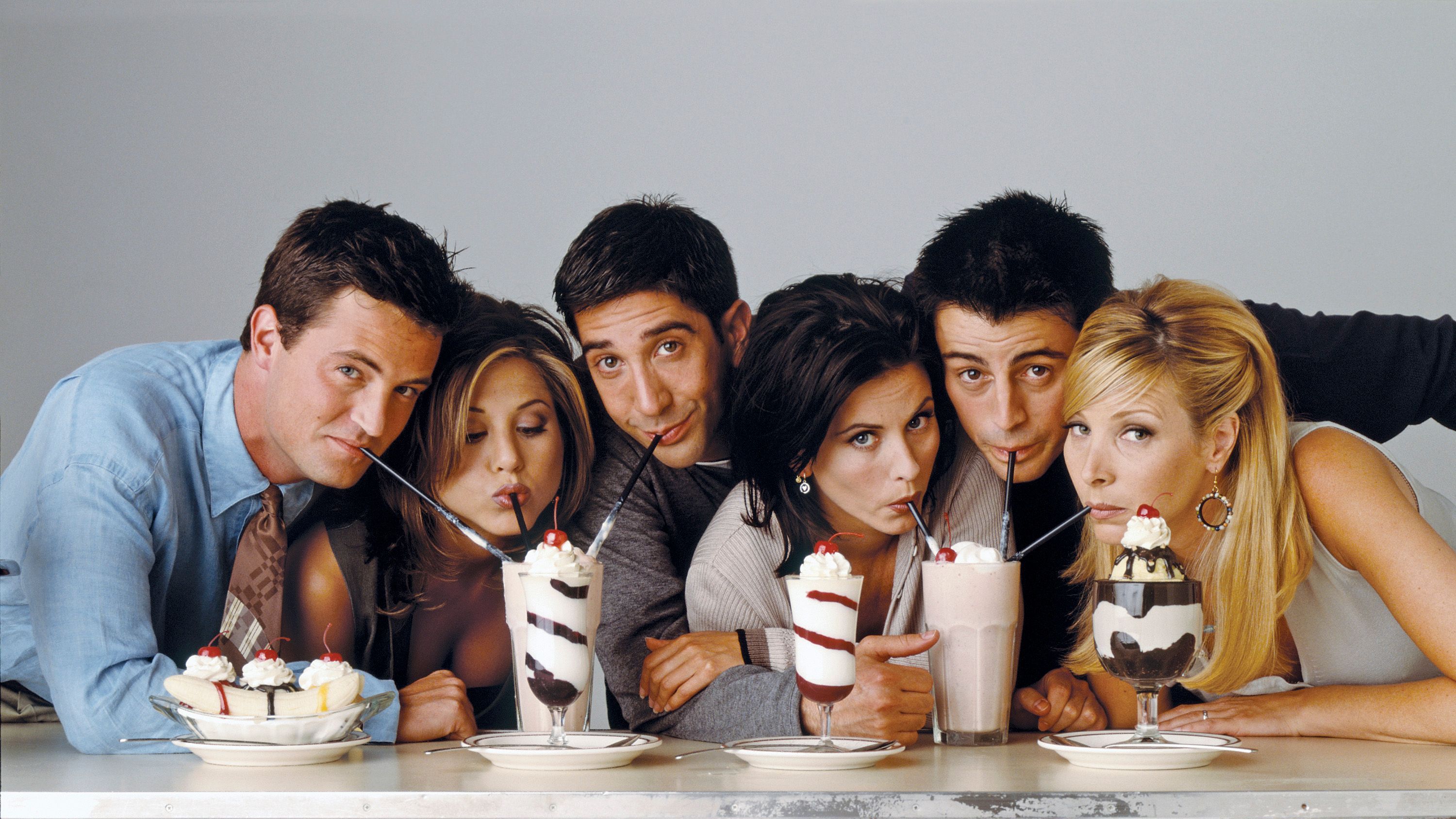 Venner - De seks venner sidder med hver deres sugerør og deler to milkshakes.