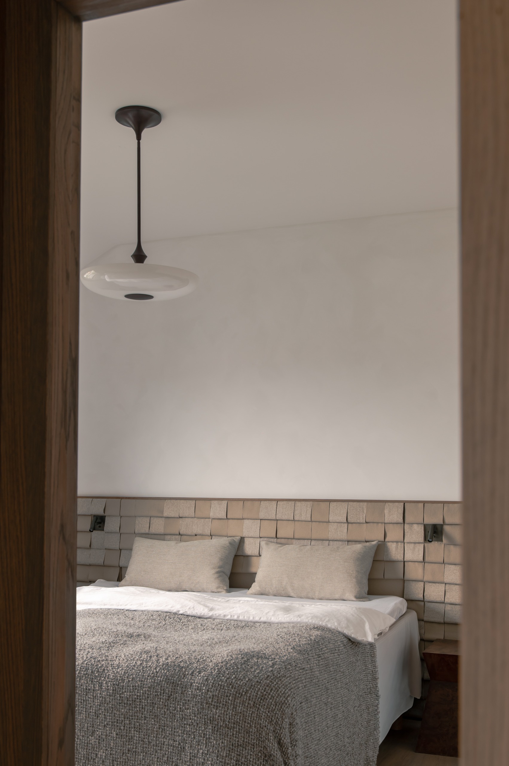 a neutral bedroom with tiled headboard and a pendant light over the bed