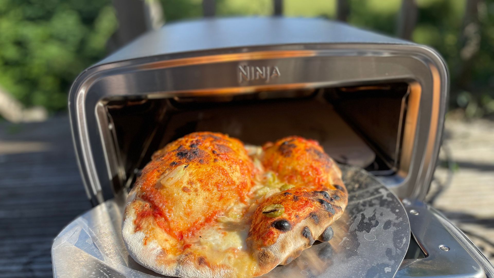 Pizza coming out of Ninja Artisan Electric Outdoor Pizza Oven and Air Fryer
