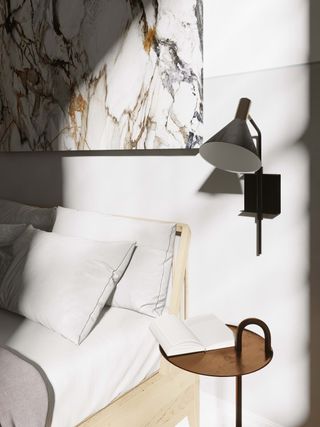 A close up of a bedside with table, lamp and artwork and lots of natural light pouring in