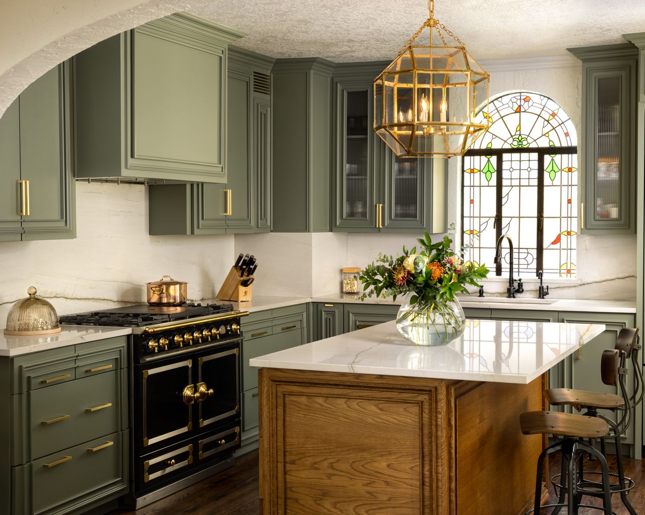 A kitchen with dark green cabinets and long, copper handles on drawers