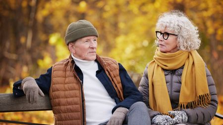 Senior couple resting on park bench in warm clothes