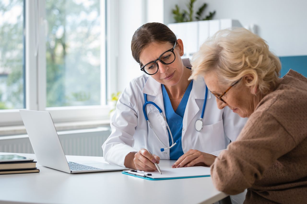 Mature adult female doctor sitting at the desk in an office and discussing test results with senior woman.