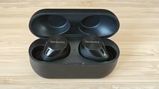 A pair of wireless Panasonic Technics EAH-AZ60M2 earbuds and a charging case on a wooden desk