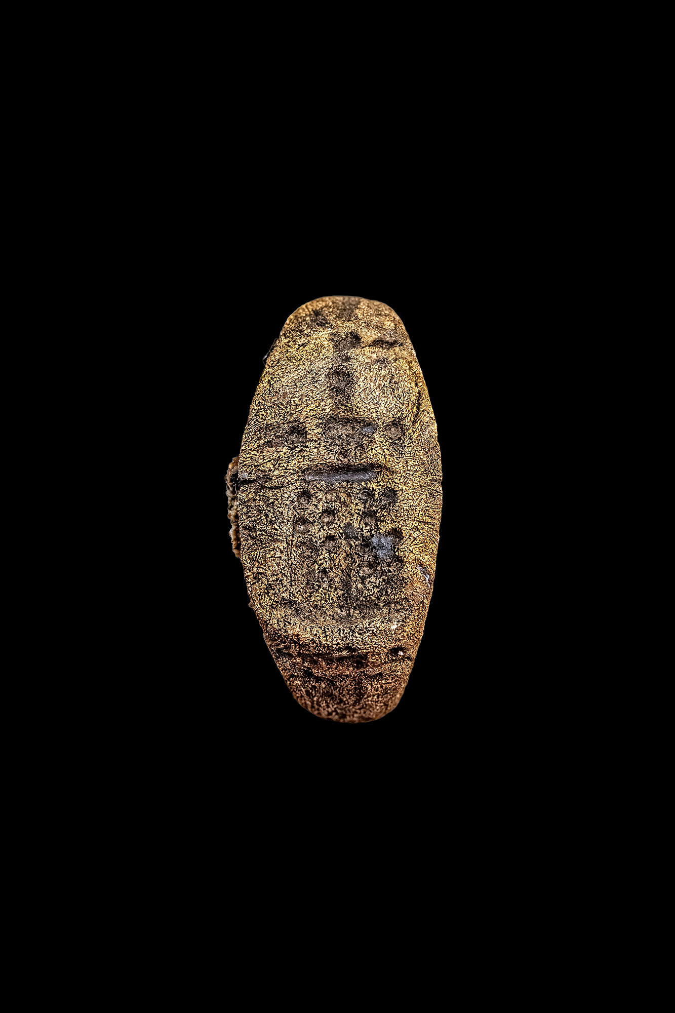 A close up of a bronze ring with engravings on it against a black background.