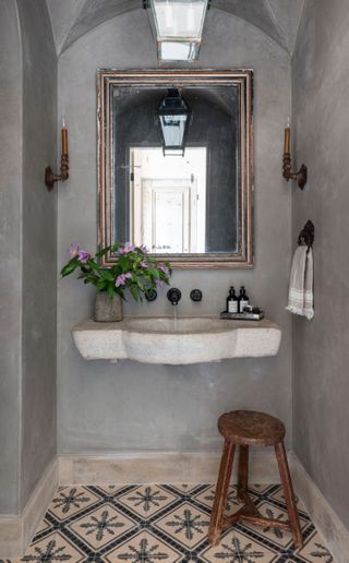 powder room with concrete walls and patterned tiled floor stone wallmounted sink and rustic wooden stool