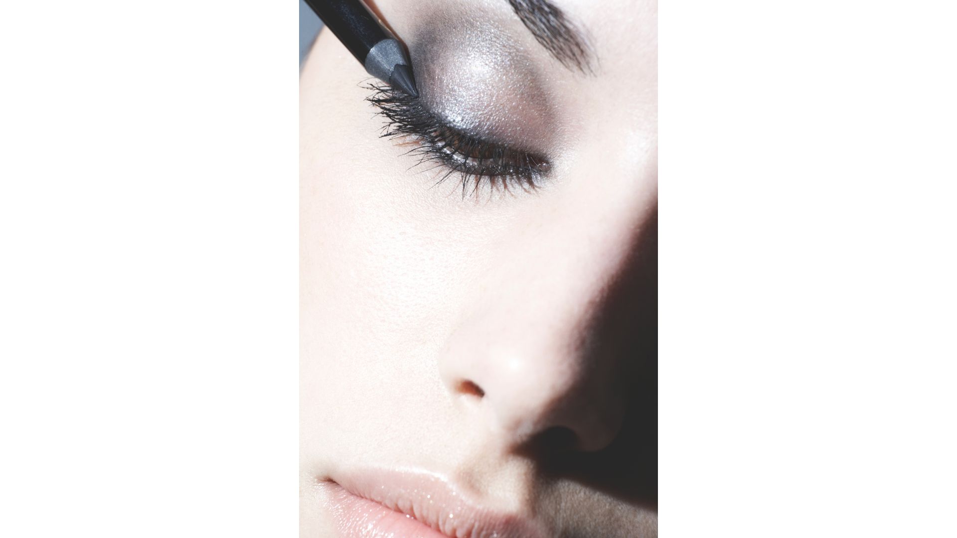 A woman's face, close up with a blue backdrop, applying eyeshadow on a smoky eye