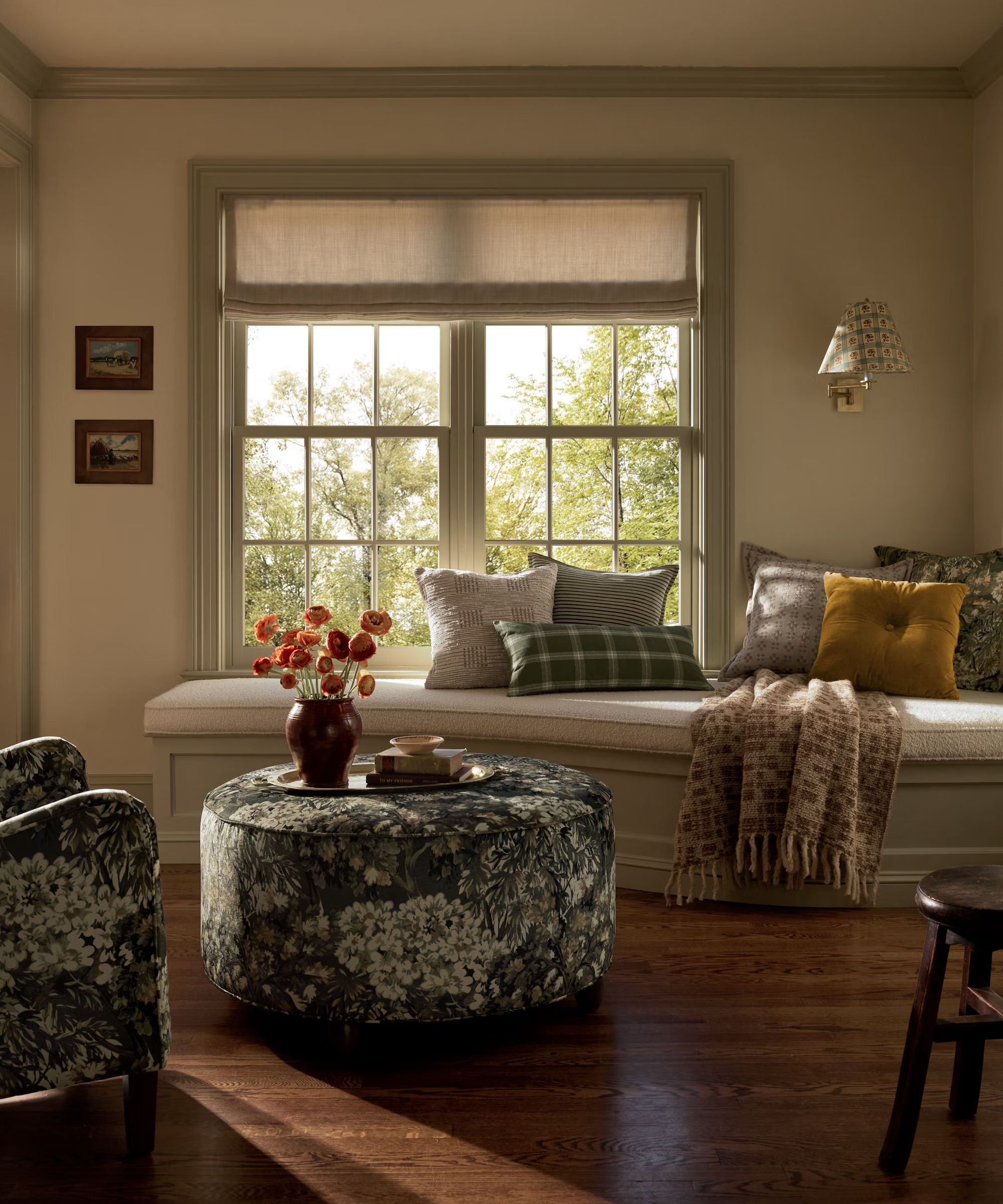 banquette window seat styled for fall with a green tapestry print armchair and ottoman, styled with a tray with books and a vase of orange dried flowers and a mix of fall pillows and blankets