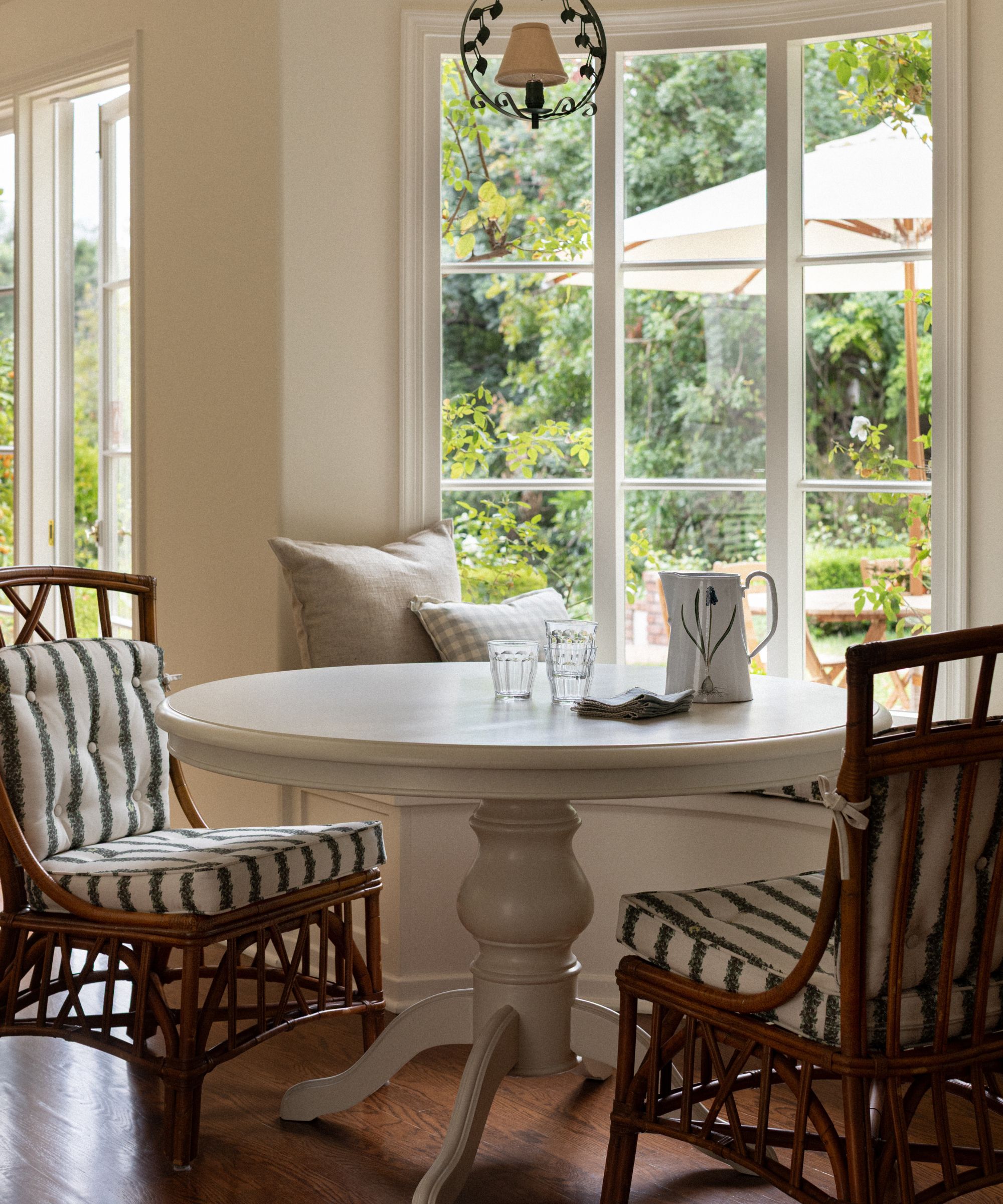 a small breakfast nook with a round table, two rattan chairs and a curved banquette plus a large window and doors with views out to the garden