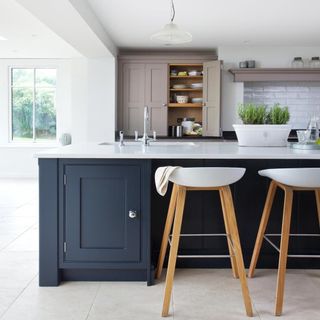 kitchen with white wall navy blue cabinets white counter and wooden bar stools
