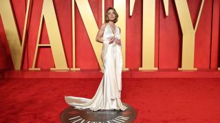 Sydney Sweeney posing for a photo at the 2024 Vanity Fair Oscar Party on the red carpet wearing a white dress.