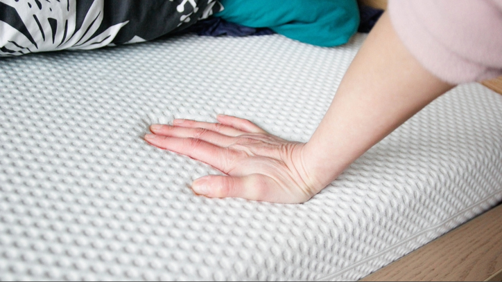 A hand pressing into a white mattress.