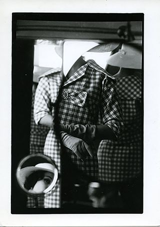 a black and white abstract image showing mirrors and an individual wearing a checkered suit and gloves