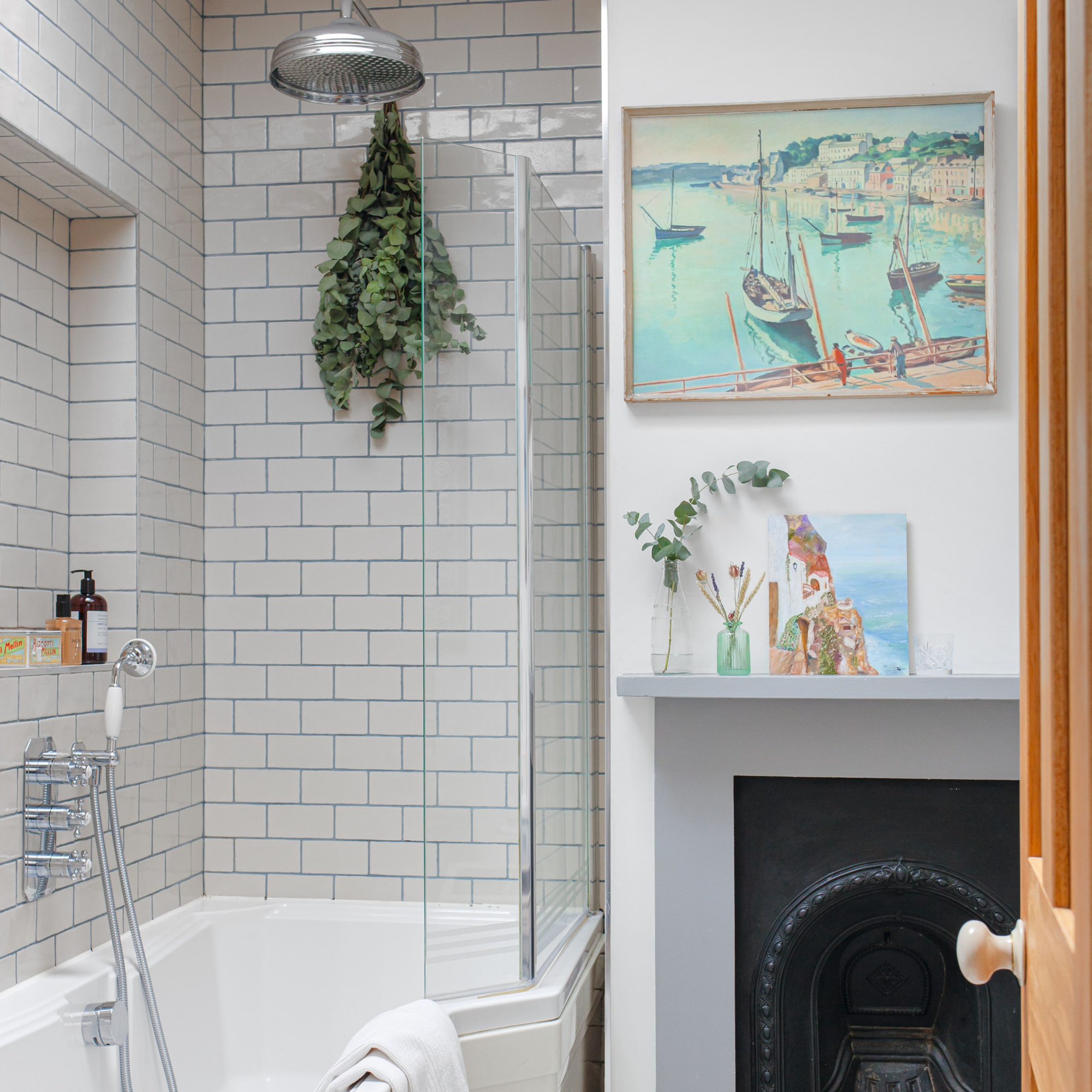 Tiled bathroom and bathtub shower, next to fireplace and hanging artwork