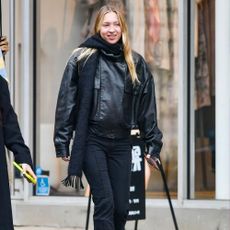 Lila Moss wears black flared trousers with a black leather jacket and heeled boots.