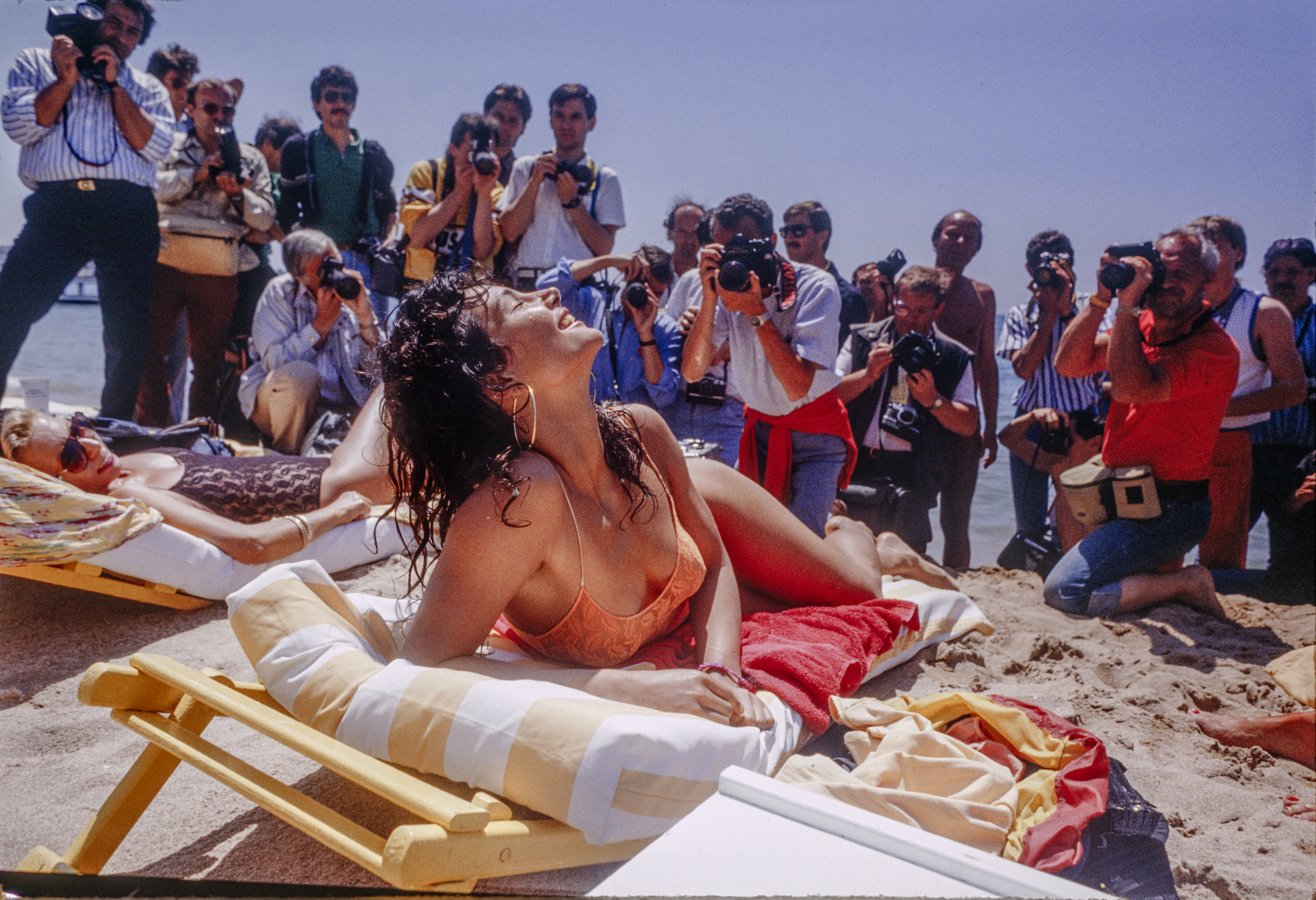 Laughing model in swimwear on beach surrounded by photographers