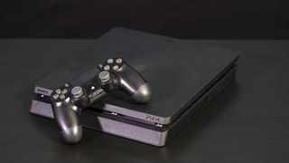 En svart PlayStation 4 Slim ligger på en svart yta, med en tillhörande handkontroller som ligger lutad över ena sidan på spelkonsolen.