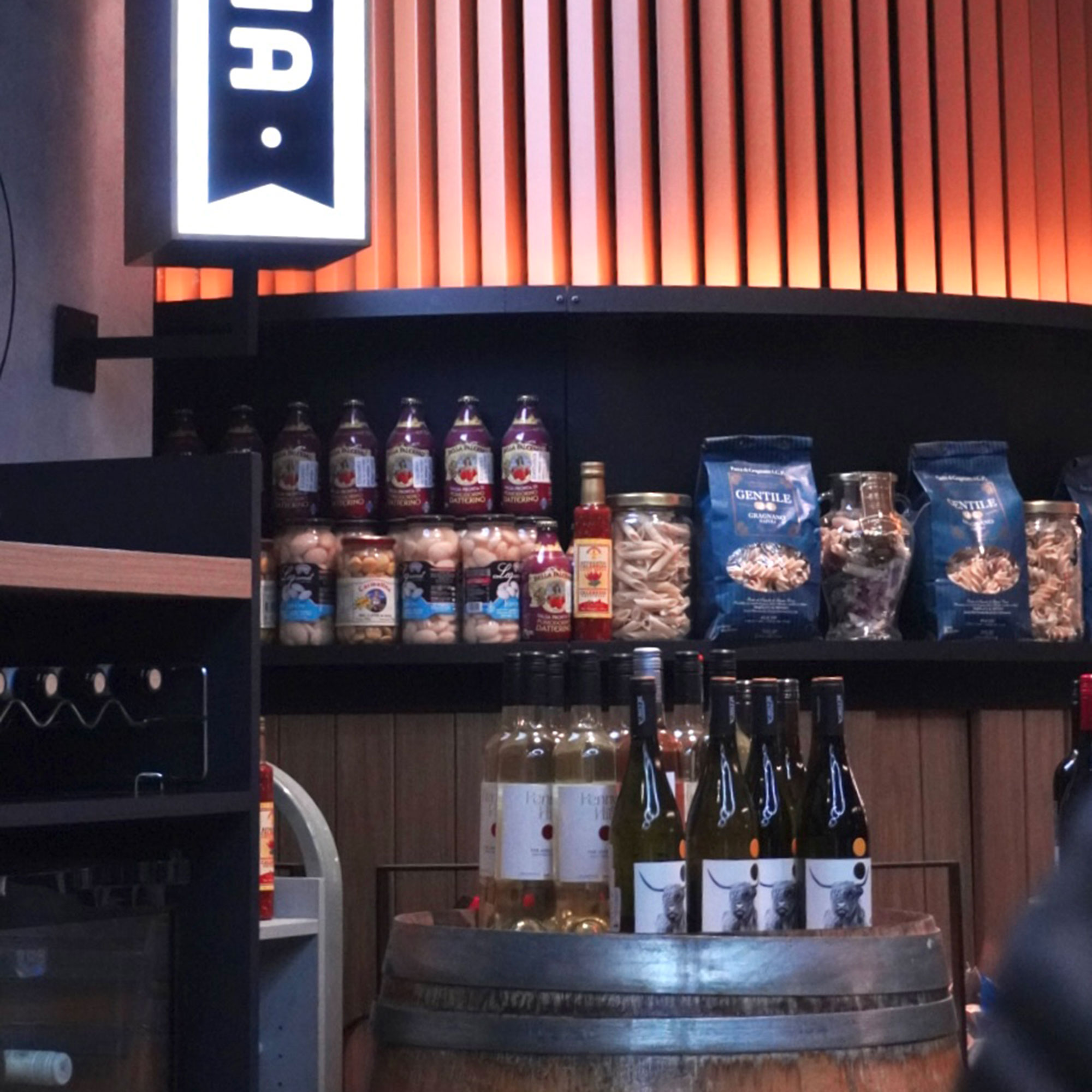 Bar with wine bottle on wooden barrel and jars and bags of snacks on rounded open shelf