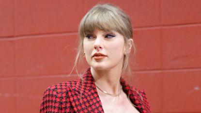 Taylor Swift wears a red and black houndstooth jacket, a black corset, and red lipstick