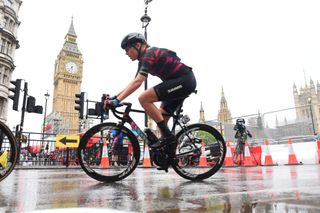 A pro rider races in the rain with a Elizabeth Tower and railing in the background.