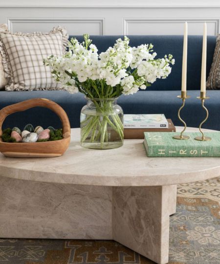 living room with a navy blue couch and a marble round coffee table decorated for easter with flowers and a wooden basket filled with decorative easter eggs