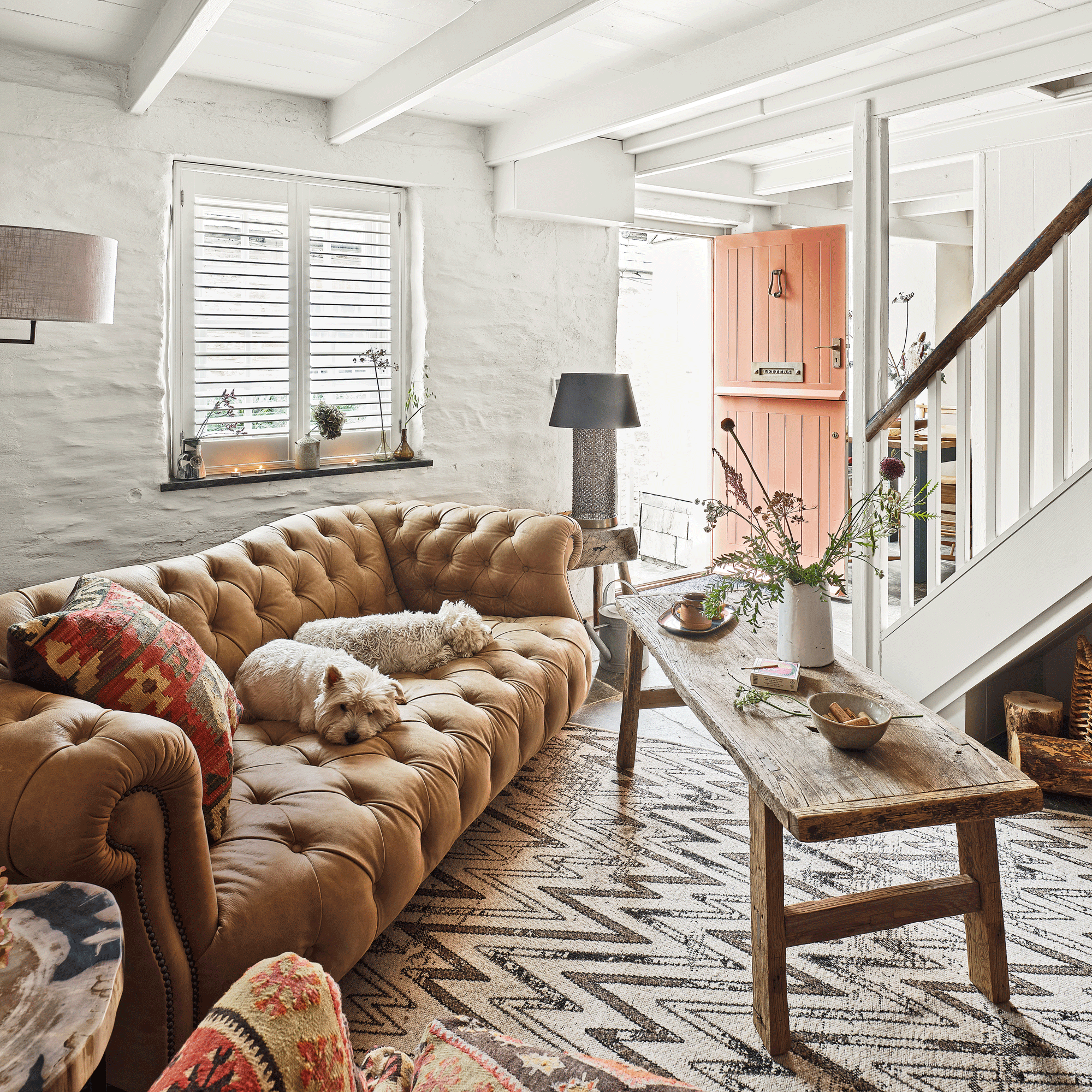 the entrance to a home with a living area just inside the front door with a large chesterfield style leather sofa a patterned rug and a couple of sleeping dogs