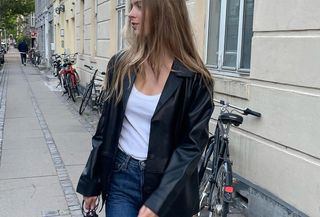 Woman wearing white t-shirt, black blazer, straight leg jeans and black bag while standing on street.