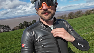 A white man in the sun wearing a short sleeve grey waterproof jersey and large mirrored sunglasses