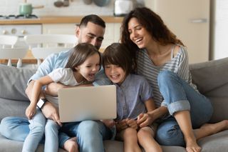 Close up happy parents with daughter and son using laptop sitting on couch at home. Smiling mother, father and cute children looking at laptop screen using video call. Family having fun with computer.