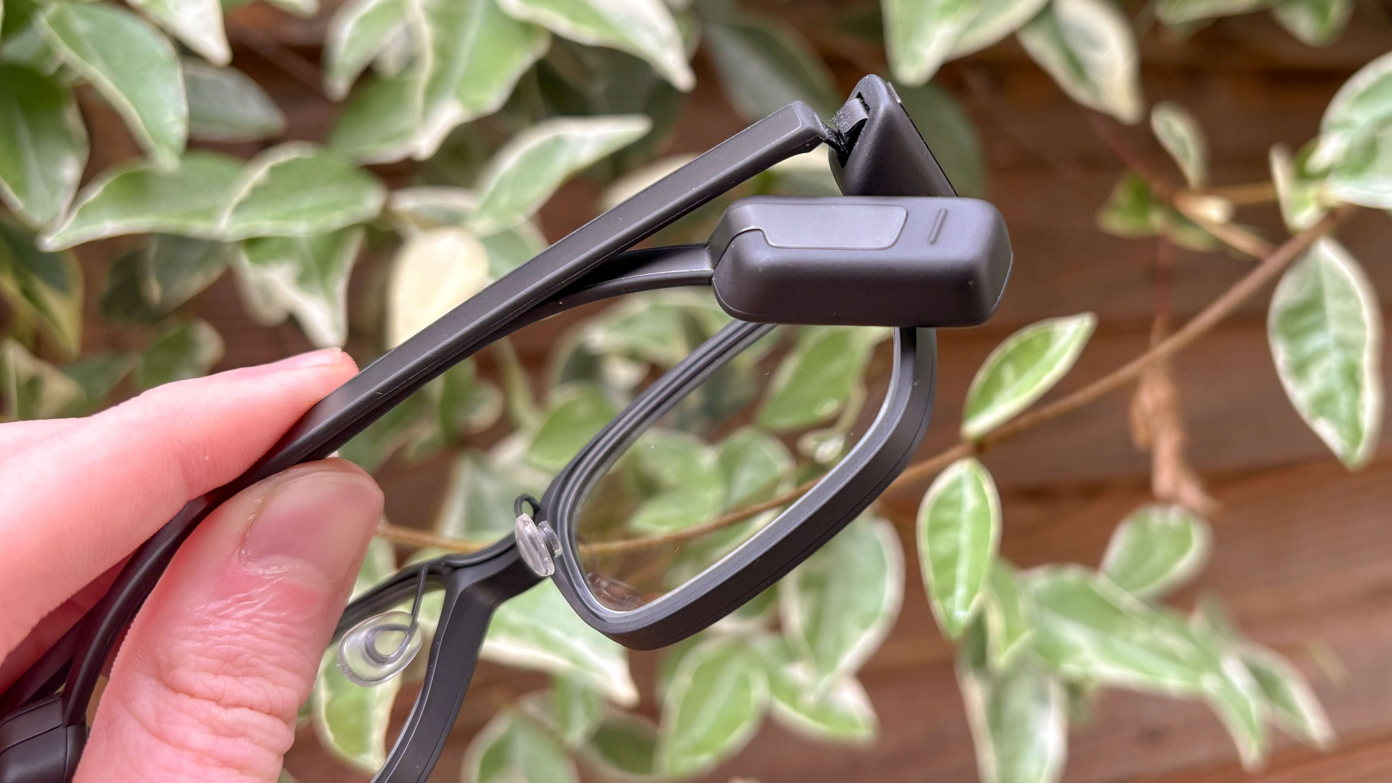 Even Realities G1 Smart Glasses held in hand showing temple tip with green leaves in background