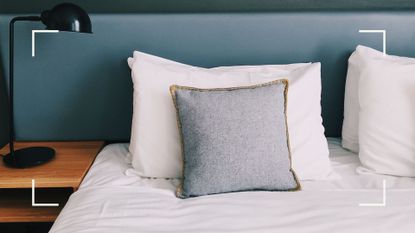 blue bedroom iwth black wall-mounted light beside a bed with freshly made white bedding to support a guide for how to wash pillows