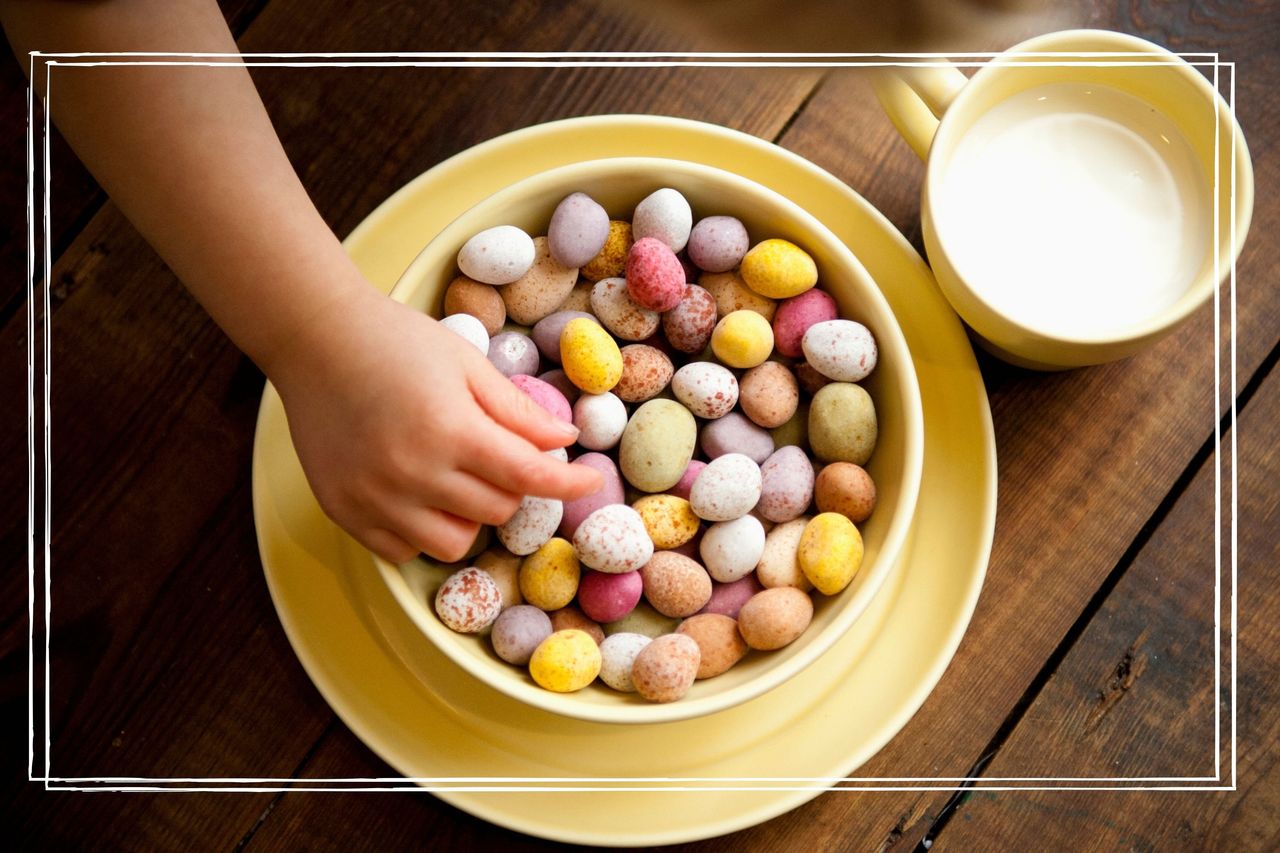 A child&#039;s hand reaching into an enormous bowl of mini eggs beside a glass of milk