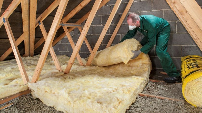 A man in a green boiler suit laying insulation in a loft
