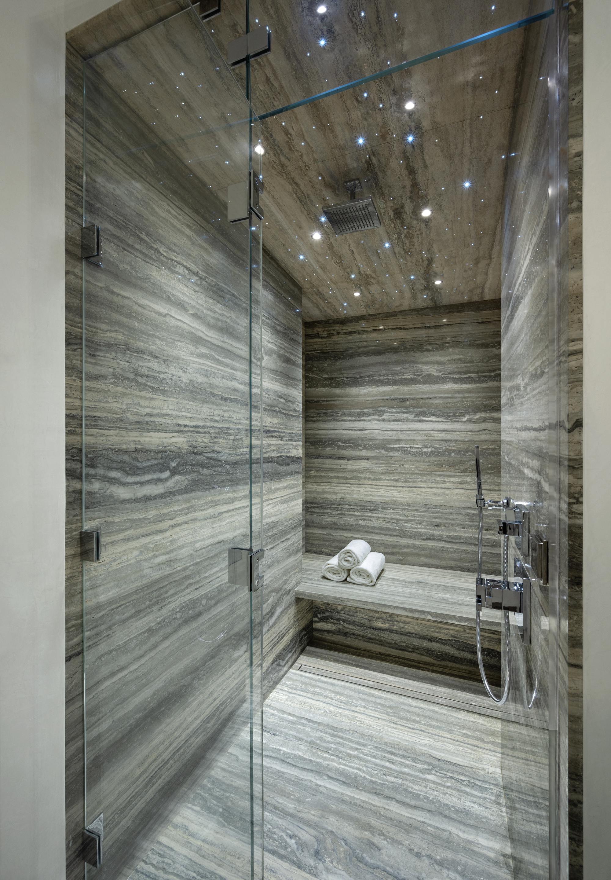 marble-drenched shower with built-in bench seat with rolled towels, silver taps and hardware, and a starry constellation on the ceiling with spotlights