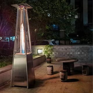 A silver pyramid shaped gas patio heater on a paved patio at night
