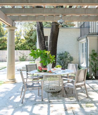 Covered outdoor eating space with table and chairs and water melon on table with pergola above