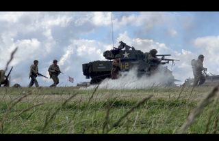 Tank on a field being followed by soldiers