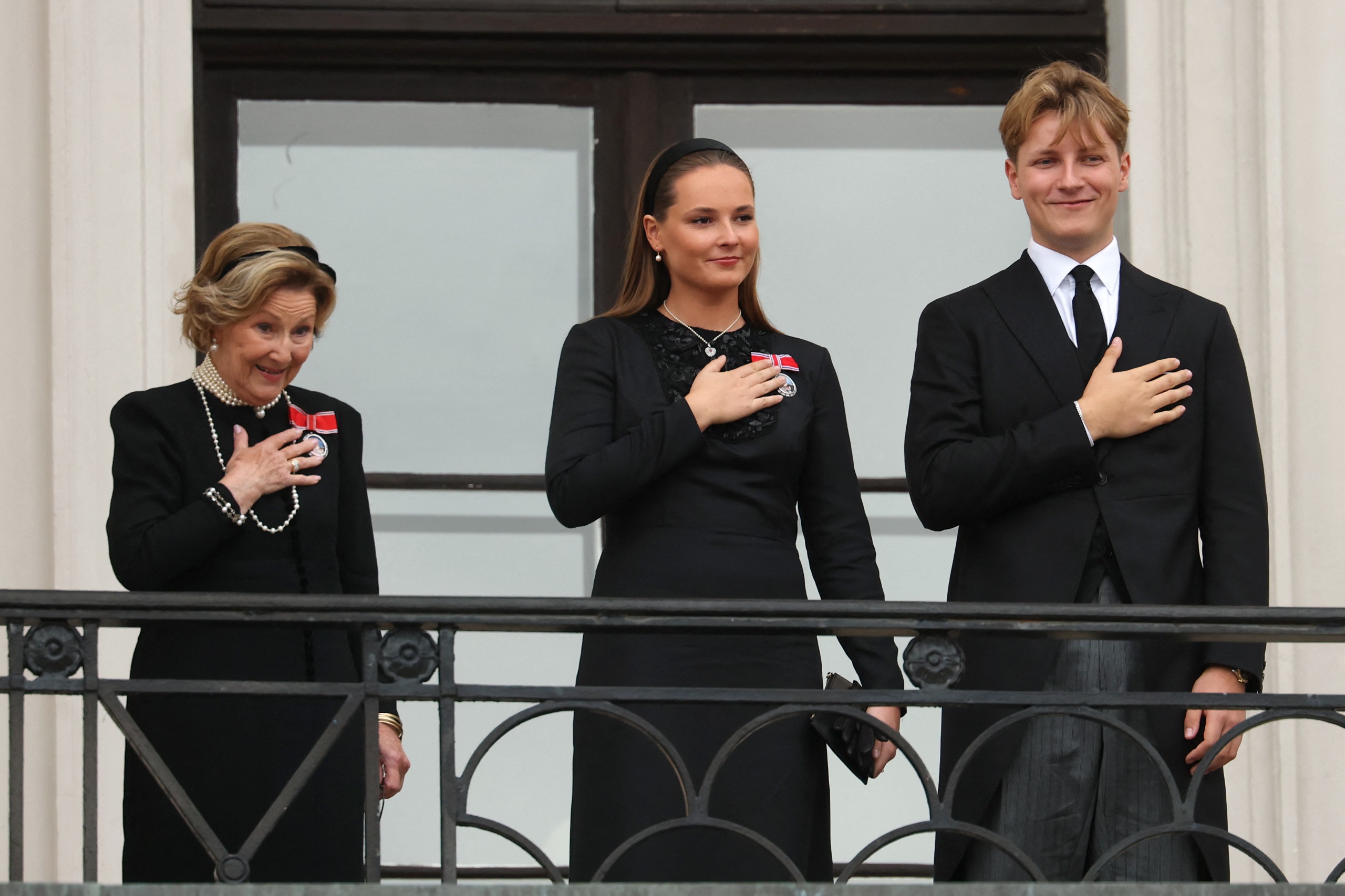 Queen Sonja, Crown Princess Ingrid Alexandra and Prince Sverre Magnus putting their hands on their hearts on the balcony after King Harald's fueneral