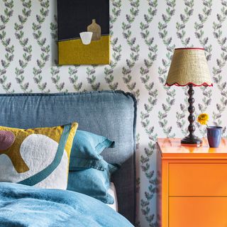 A bedroom with an upholstered headboard in navy linen, and orange bedside table and mustard accessories