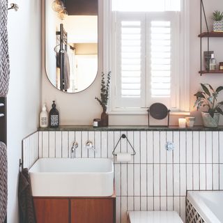 A white-tiled bathroom with an oval mirror and sink