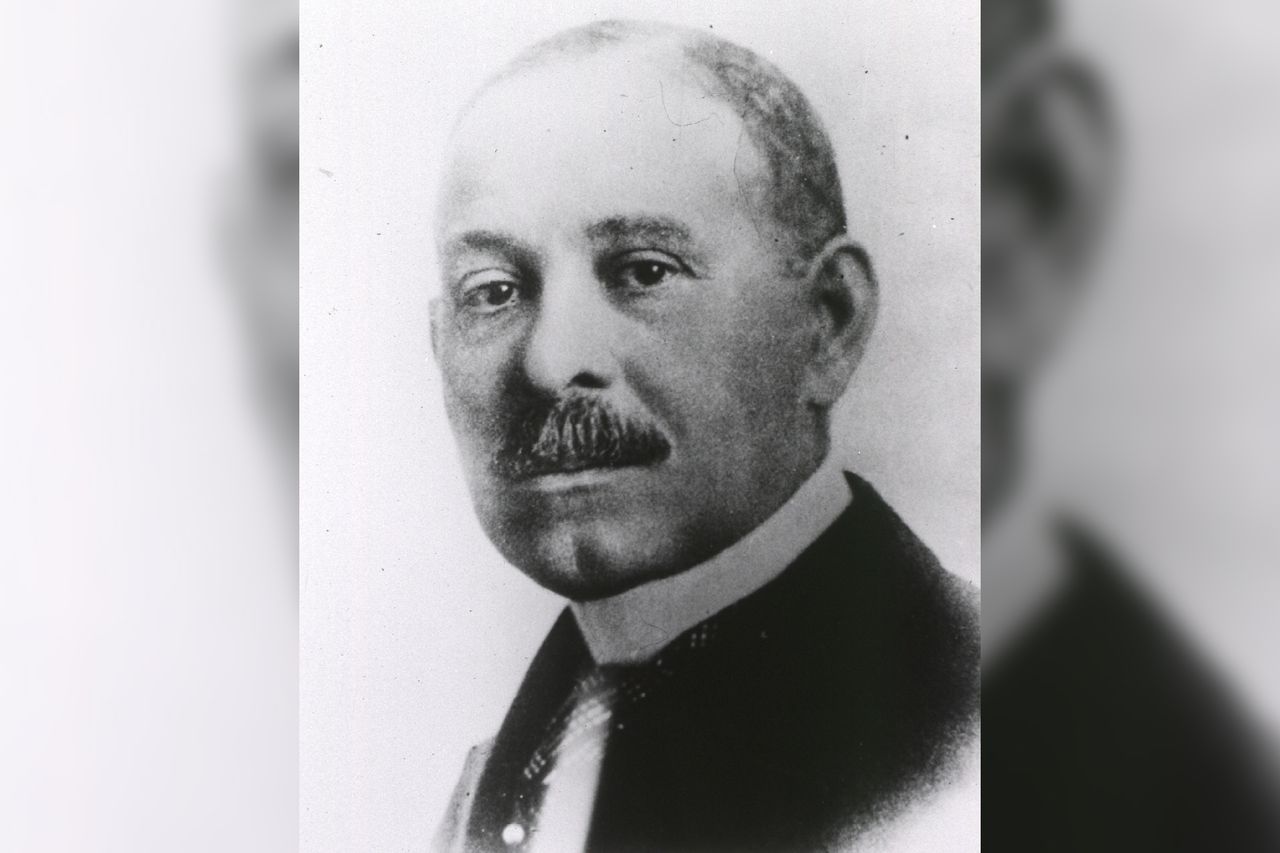 A black-and-white historic photo of a man with a moustache, looking at the camera.